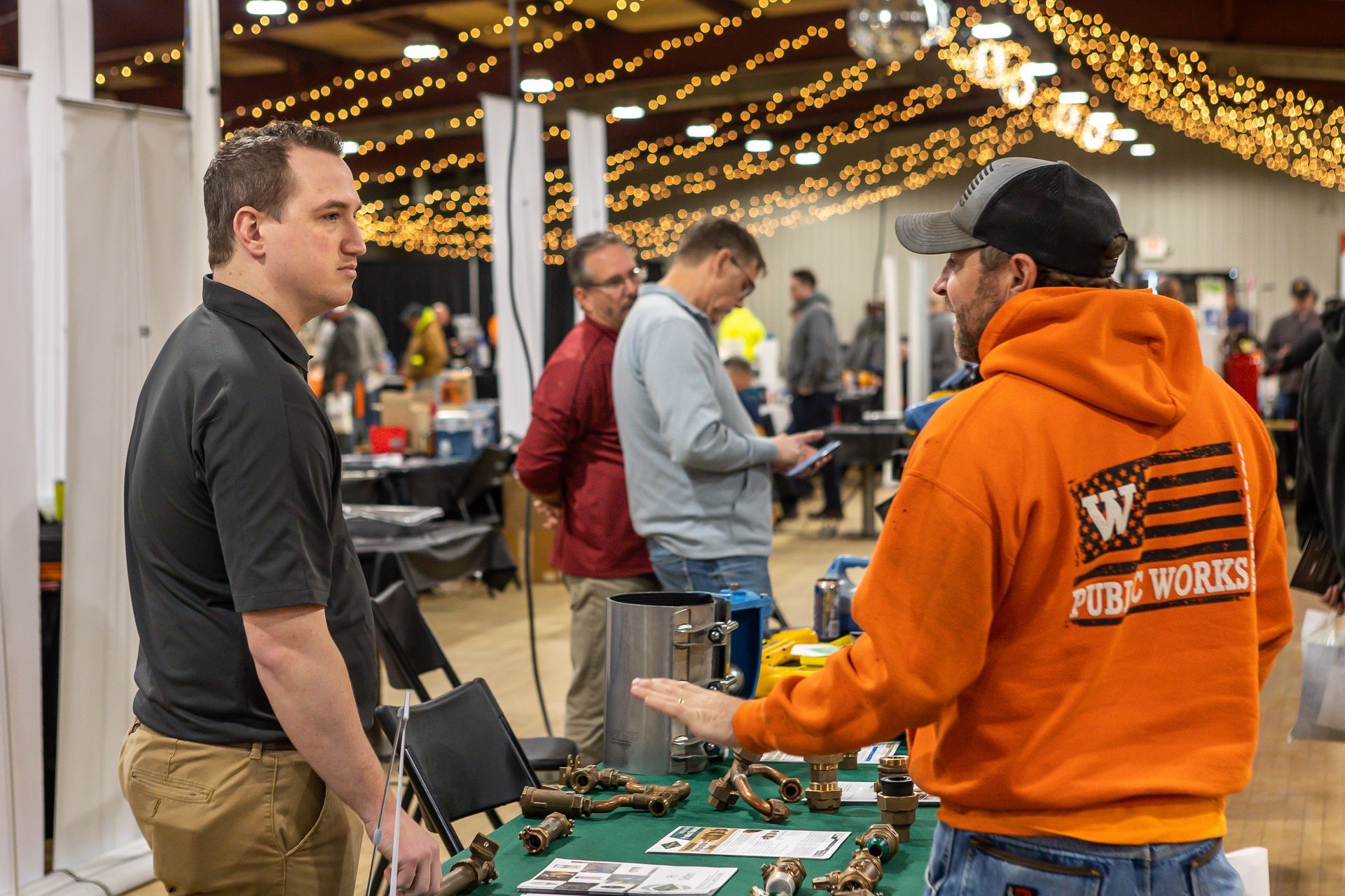 A man in an orange hoodie is talking to another man at a trade show.