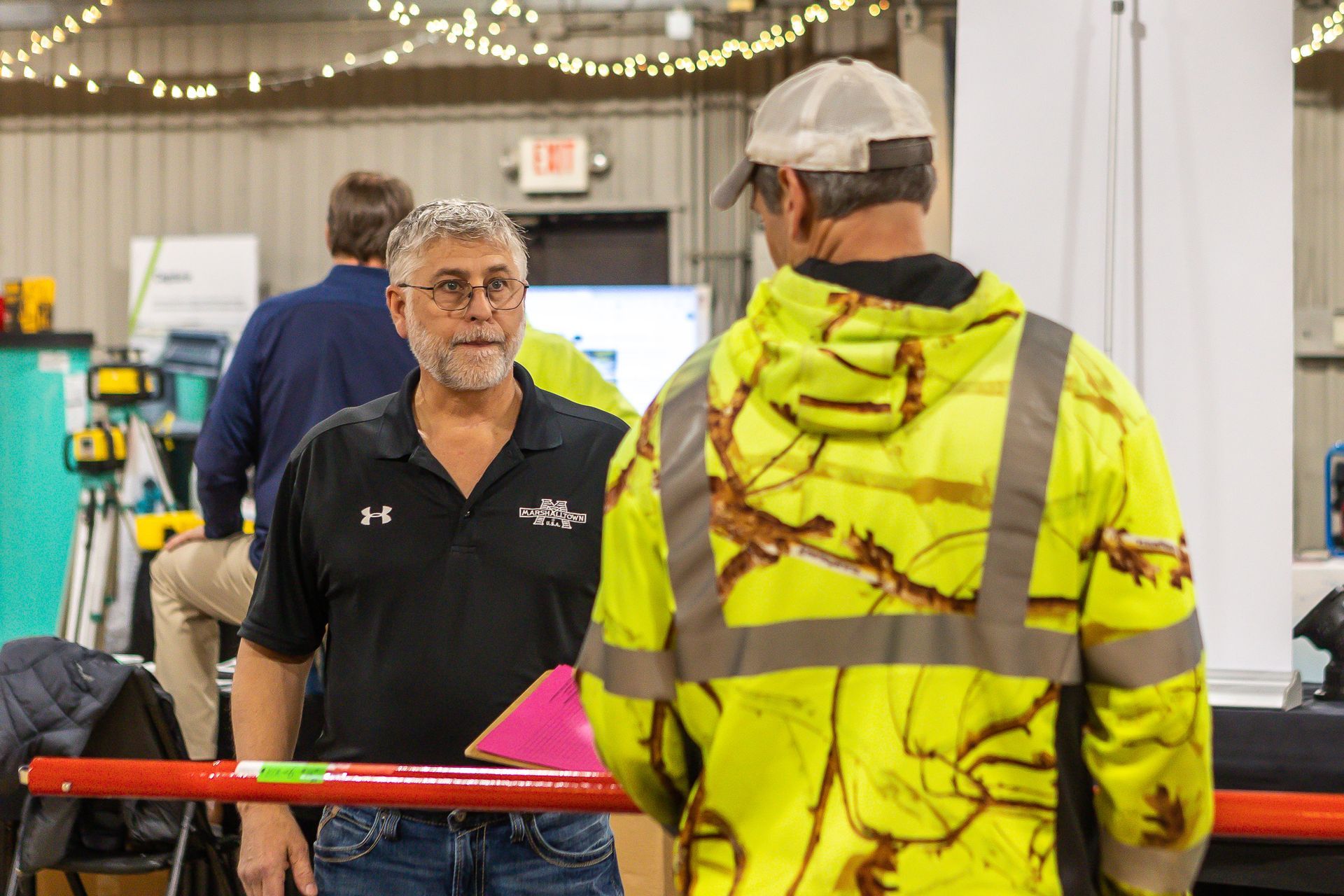 A man in a yellow jacket is talking to another man in a black shirt.