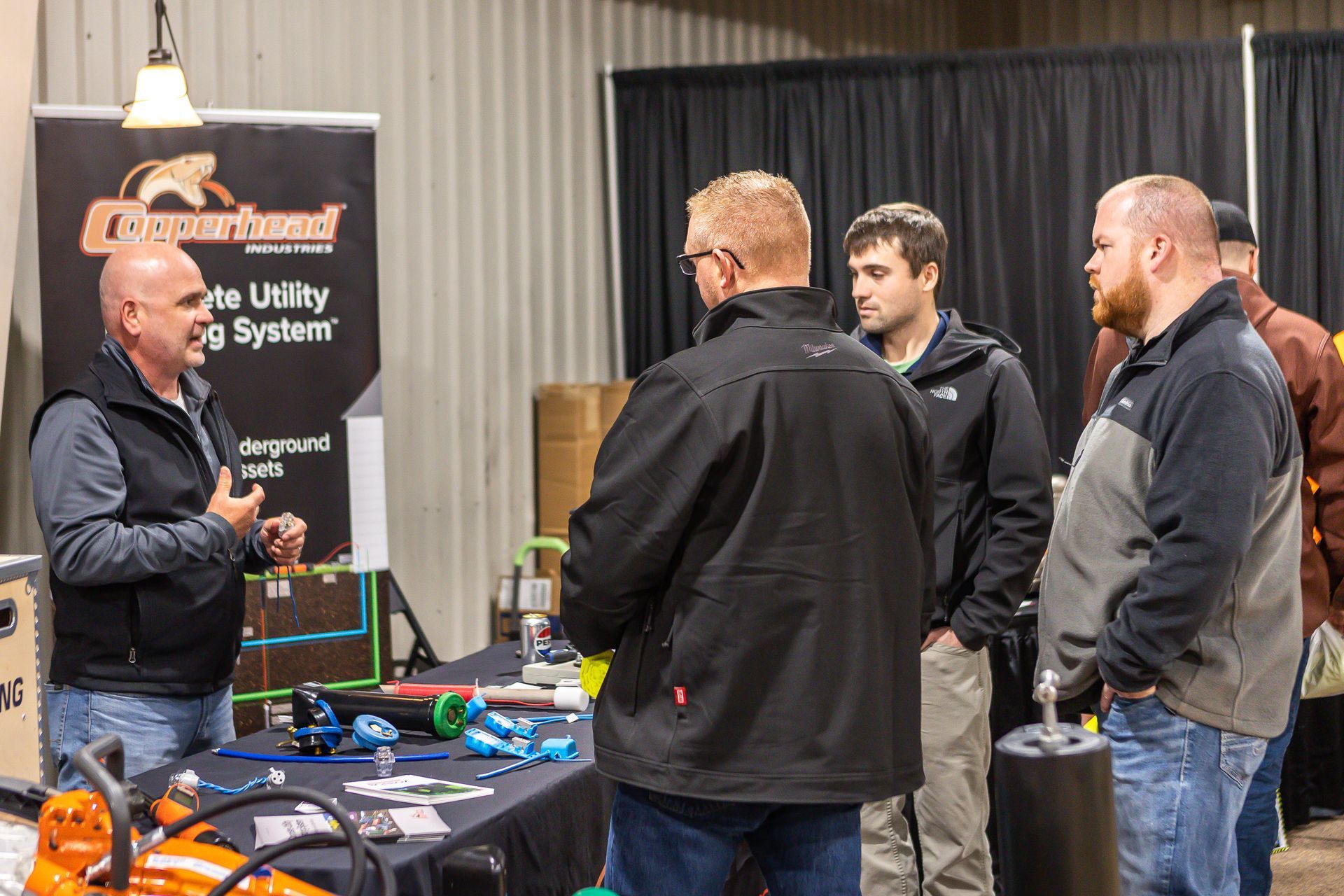 A group of men are standing around a table talking to each other.