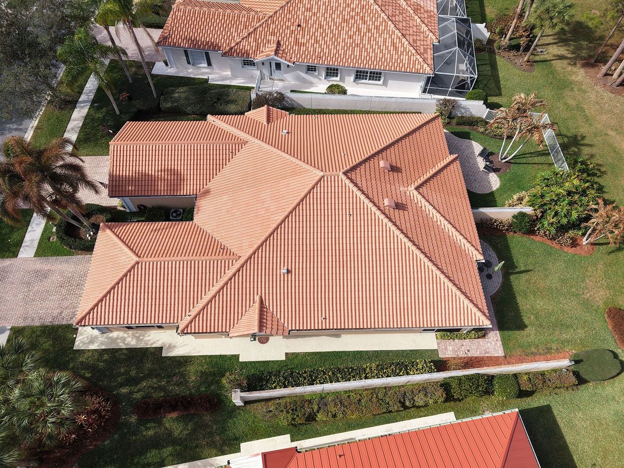 Aerial view of a residential house with a terracotta tiled roof in a sunny, landscaped neighborhood.