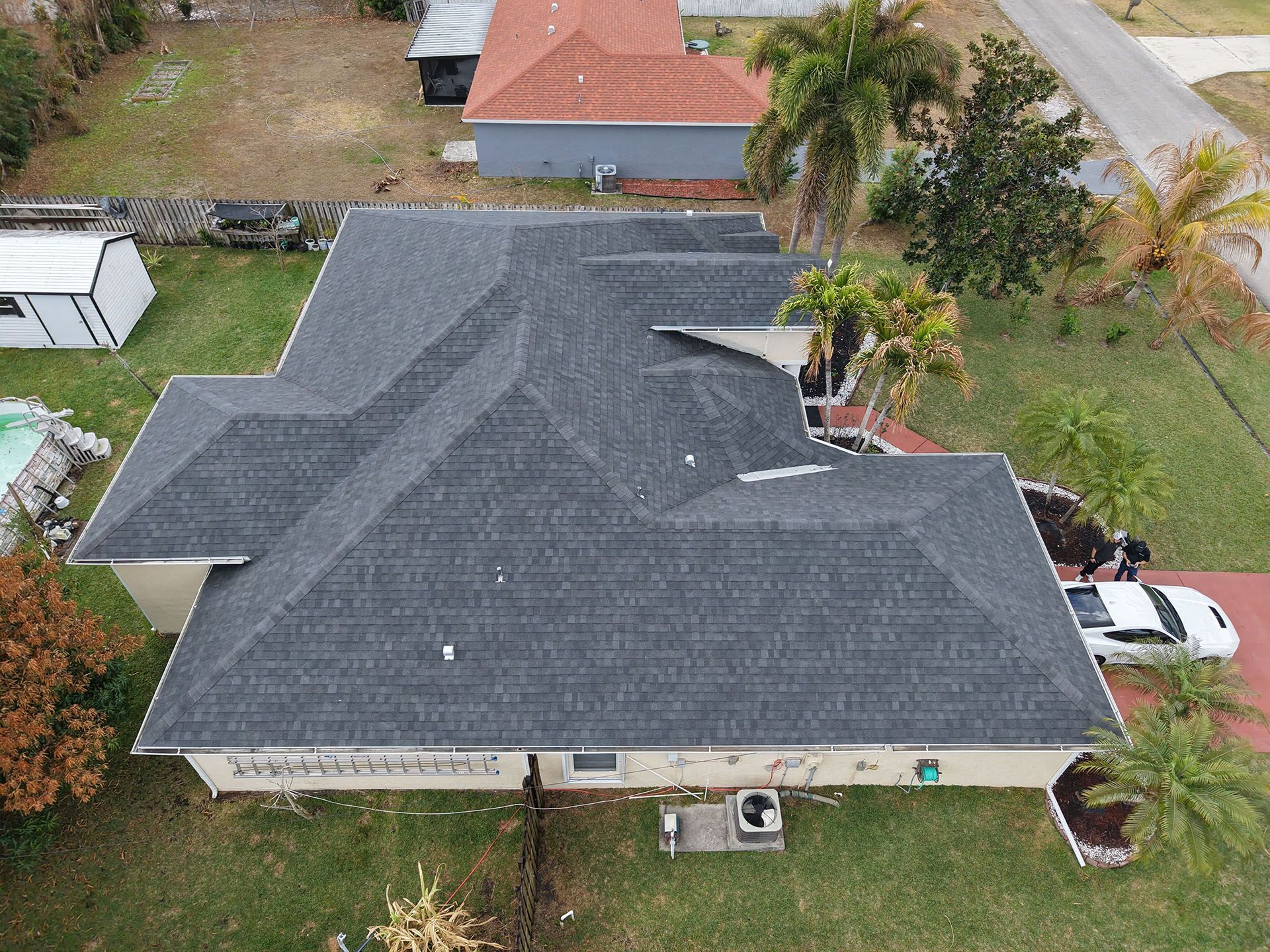 Overhead view of a house with a dark gray roof surrounded by grass and palm trees.