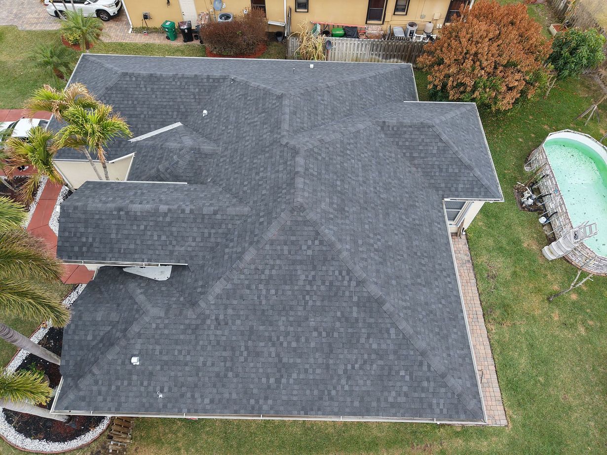 Aerial view of a gray shingled roof on a residential home with a backyard pool and landscaping nearby.