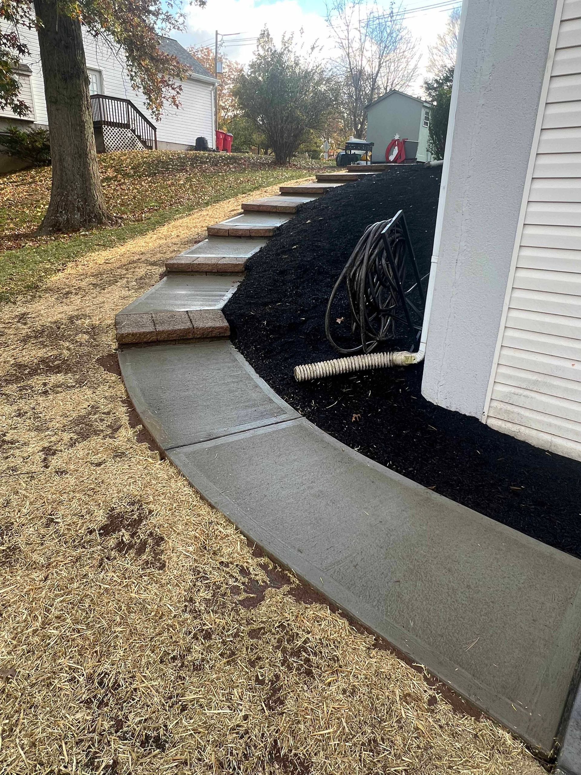 A bicycle is parked on the side of a house next to a concrete walkway.