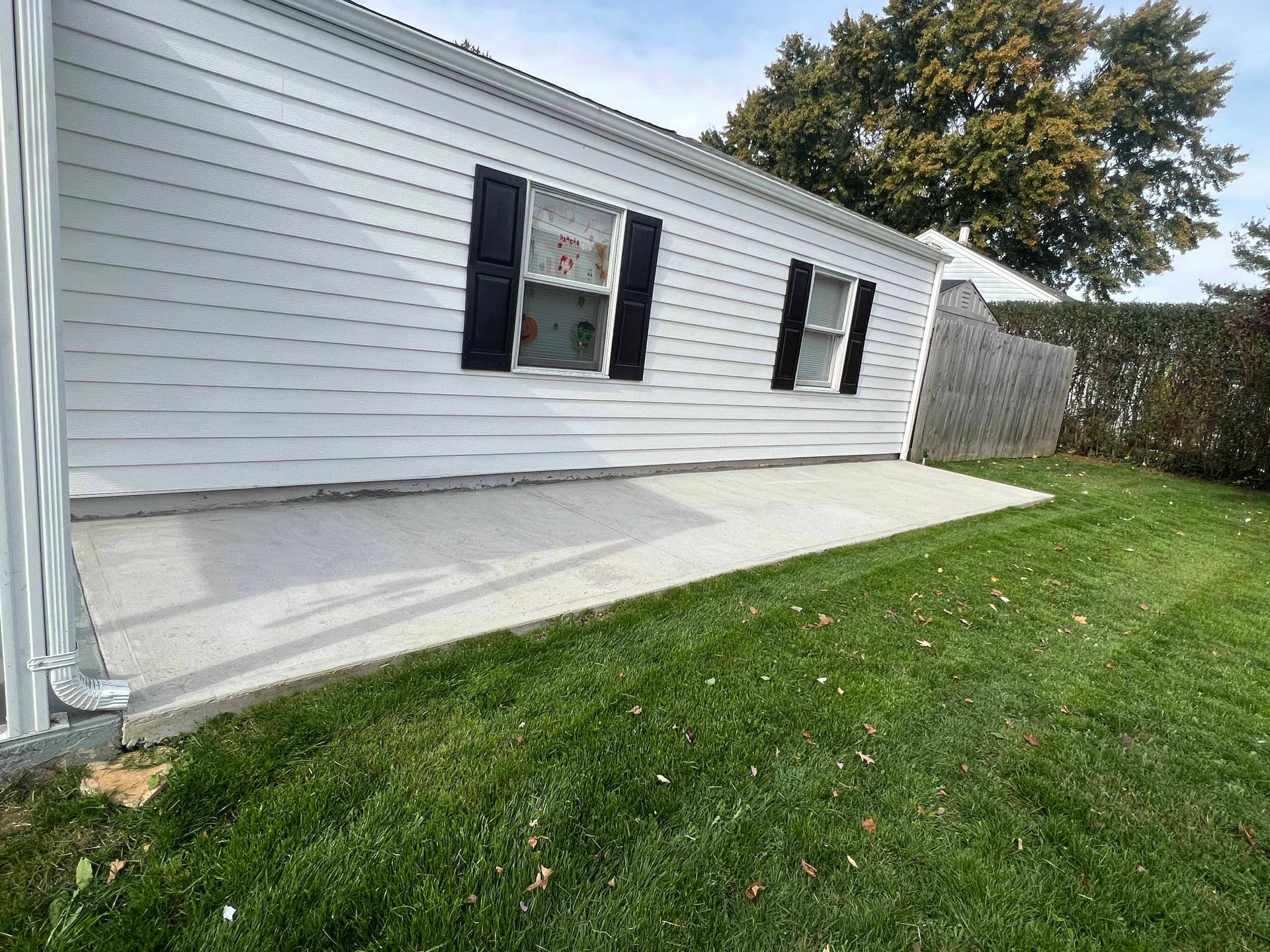 A white house with black shutters and a concrete patio in front of it.