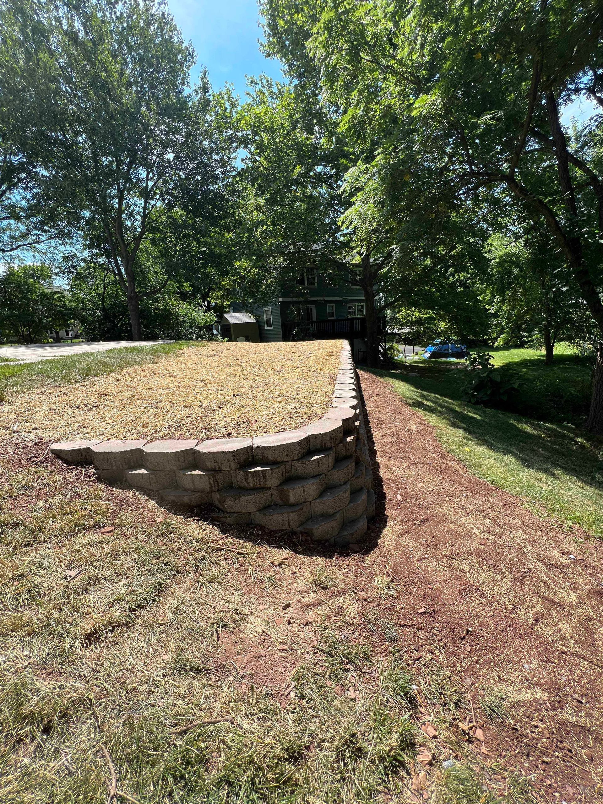 A stone wall is sitting on top of a grassy hill next to a house.