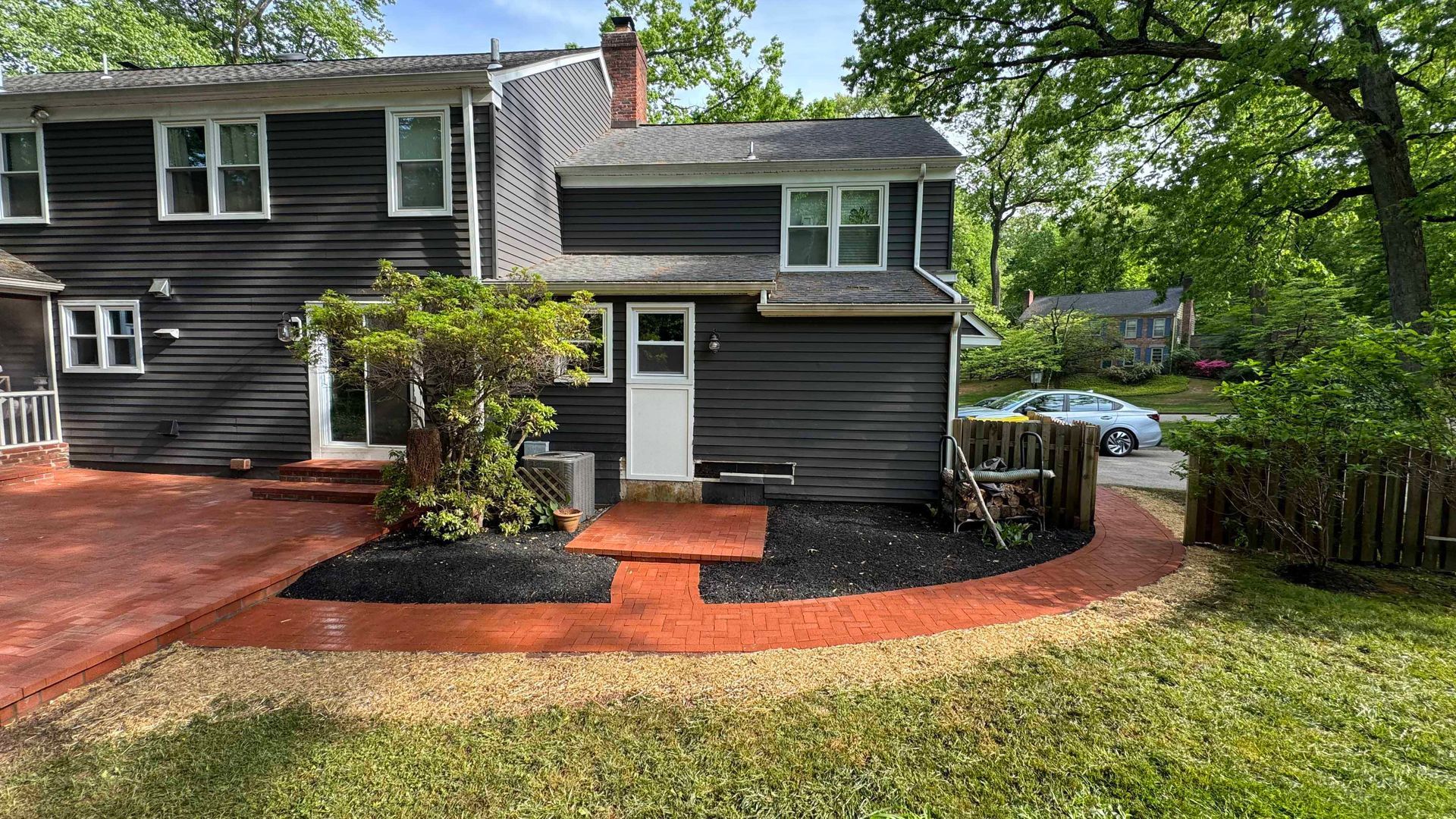 A black house with a brick driveway and a fence in front of it.