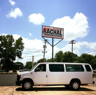 A white van is parked in front of a rachal transmissions sign