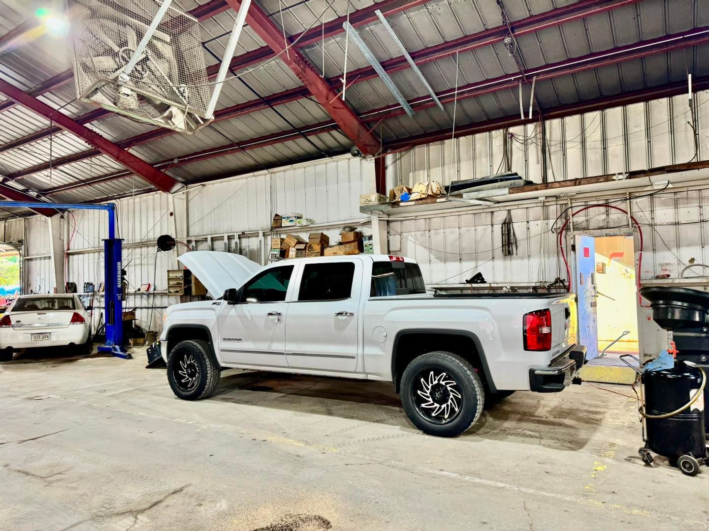 A white truck with the hood up is parked in a garage.