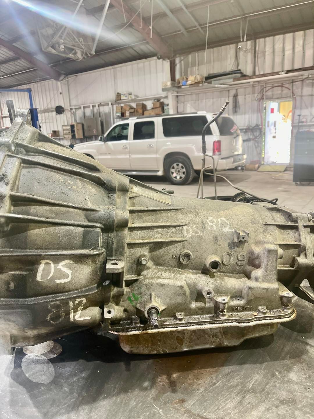 A dirty gearbox is sitting in a garage next to a white van.