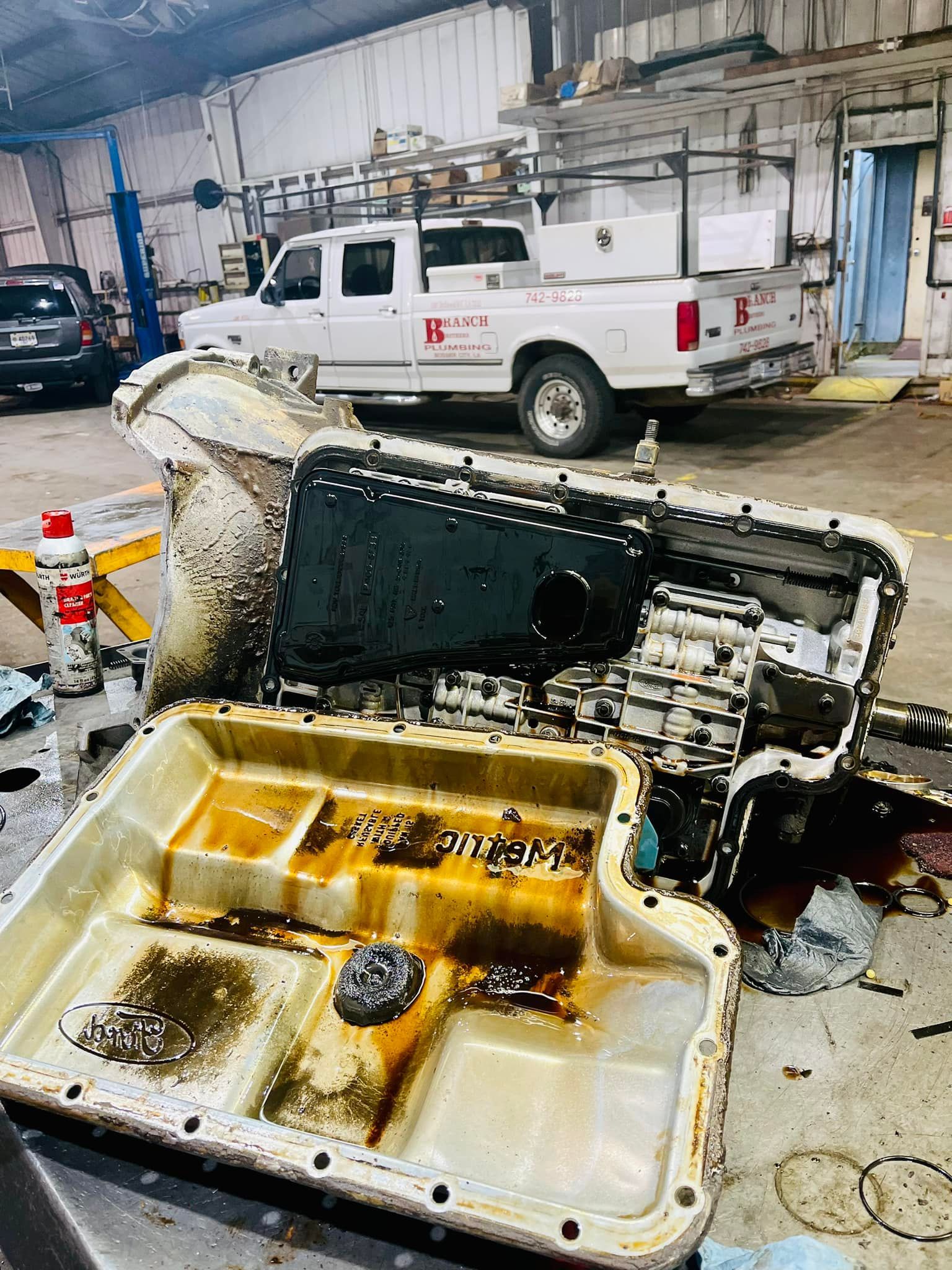 A white truck is parked in a garage next to a dirty engine.