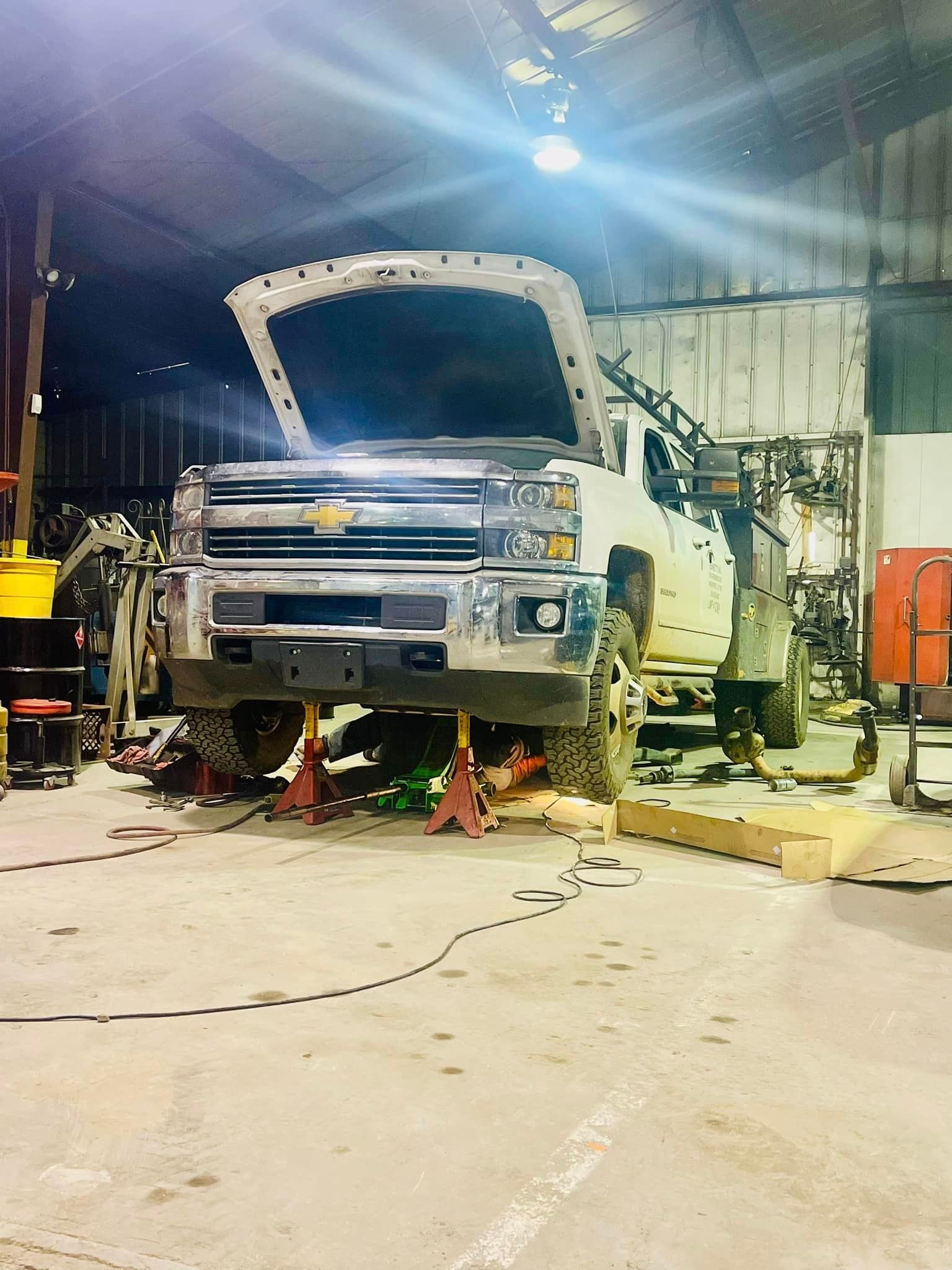 A truck is being worked on in a garage with its hood open.