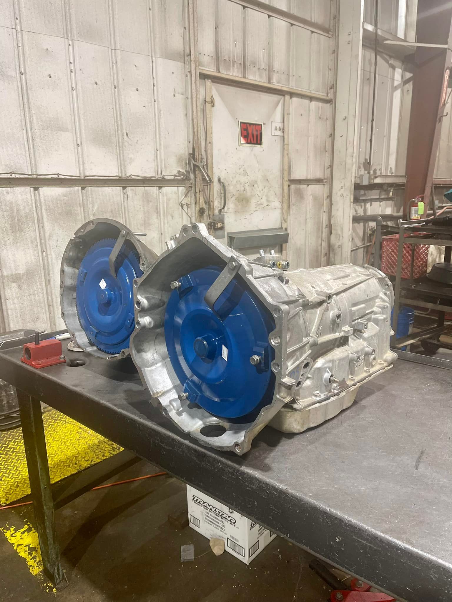 Two automatic transmissions are sitting on a table in a garage.