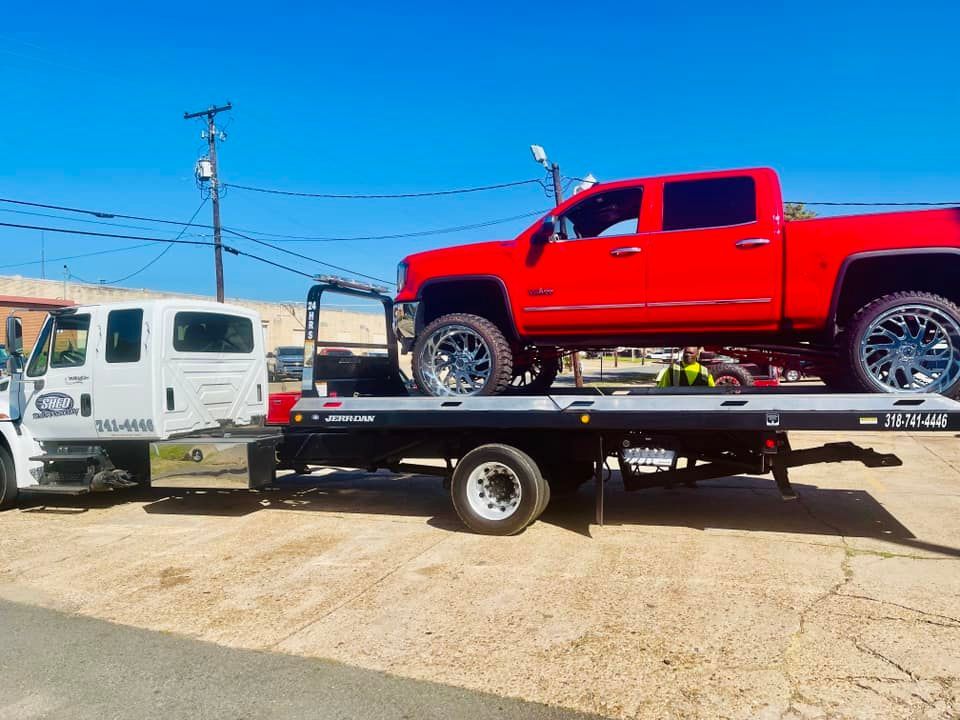 A red truck is being towed by a tow truck.