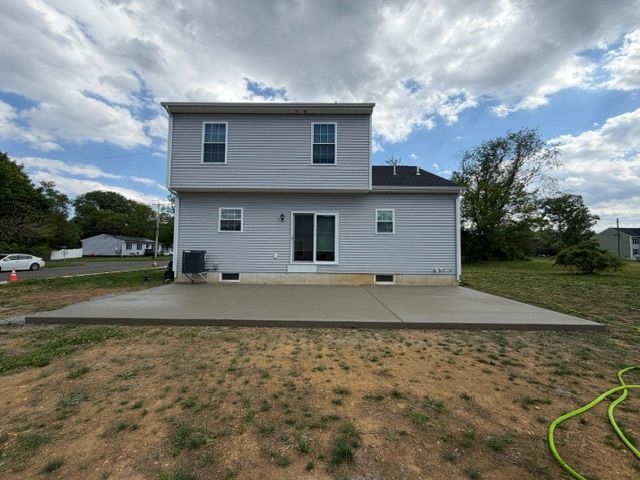 Back view of a gray two-story house with a concrete patio and grassy yard under a cloudy sky