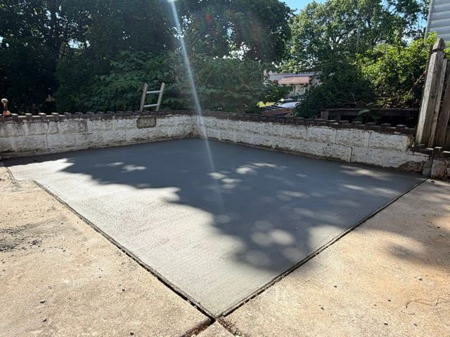 Concrete slab in a walled outdoor courtyard with trees casting shadows and a ladder leaning in back