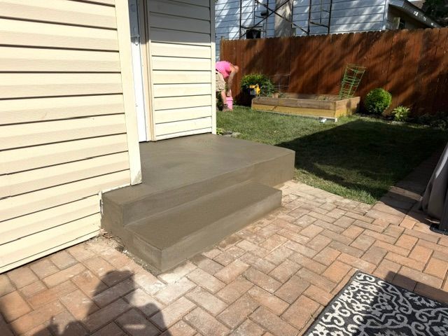 Backyard patio with brick pavers, concrete steps, and a small lawn beside a house