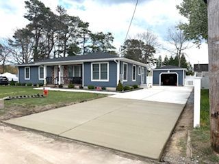 Gray single-story house with a wide concrete driveway and detached garage under a cloudy sky