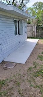 White house exterior with a concrete side ramp and a back door, beside a grassy yard