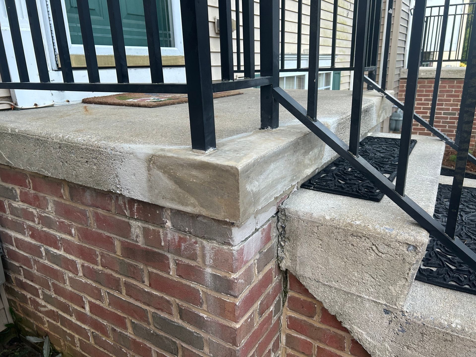 Brick and concrete porch with black railing.