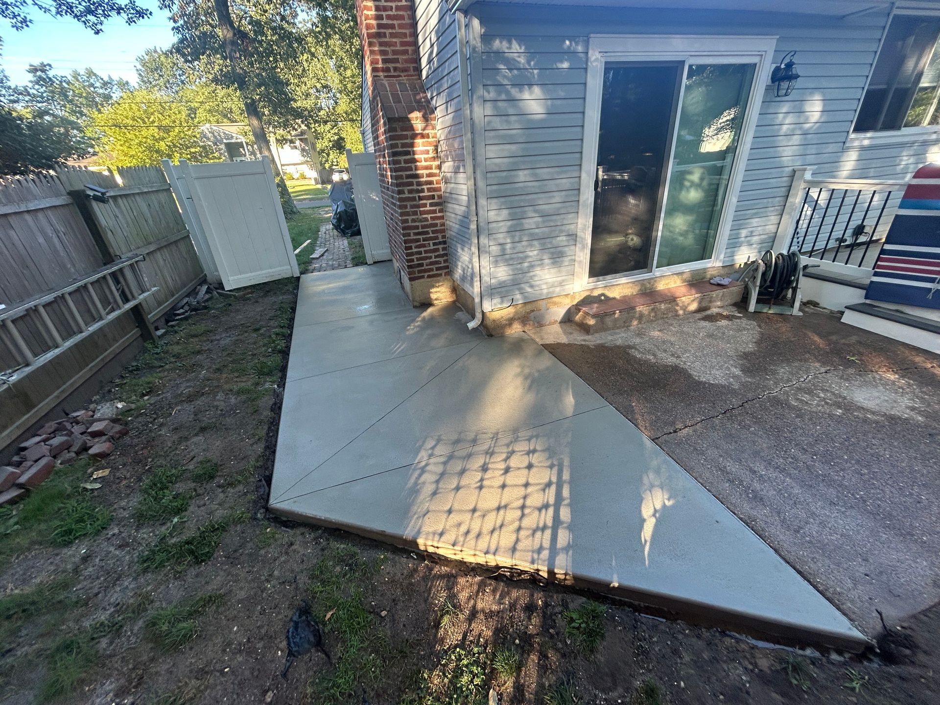Newly poured concrete patio next to a light blue house with a brick chimney.