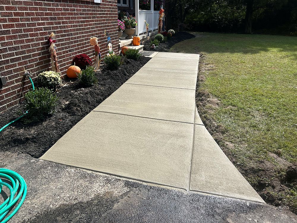 Concrete walkway leads from asphalt driveway to a brick house with decorative landscaping.