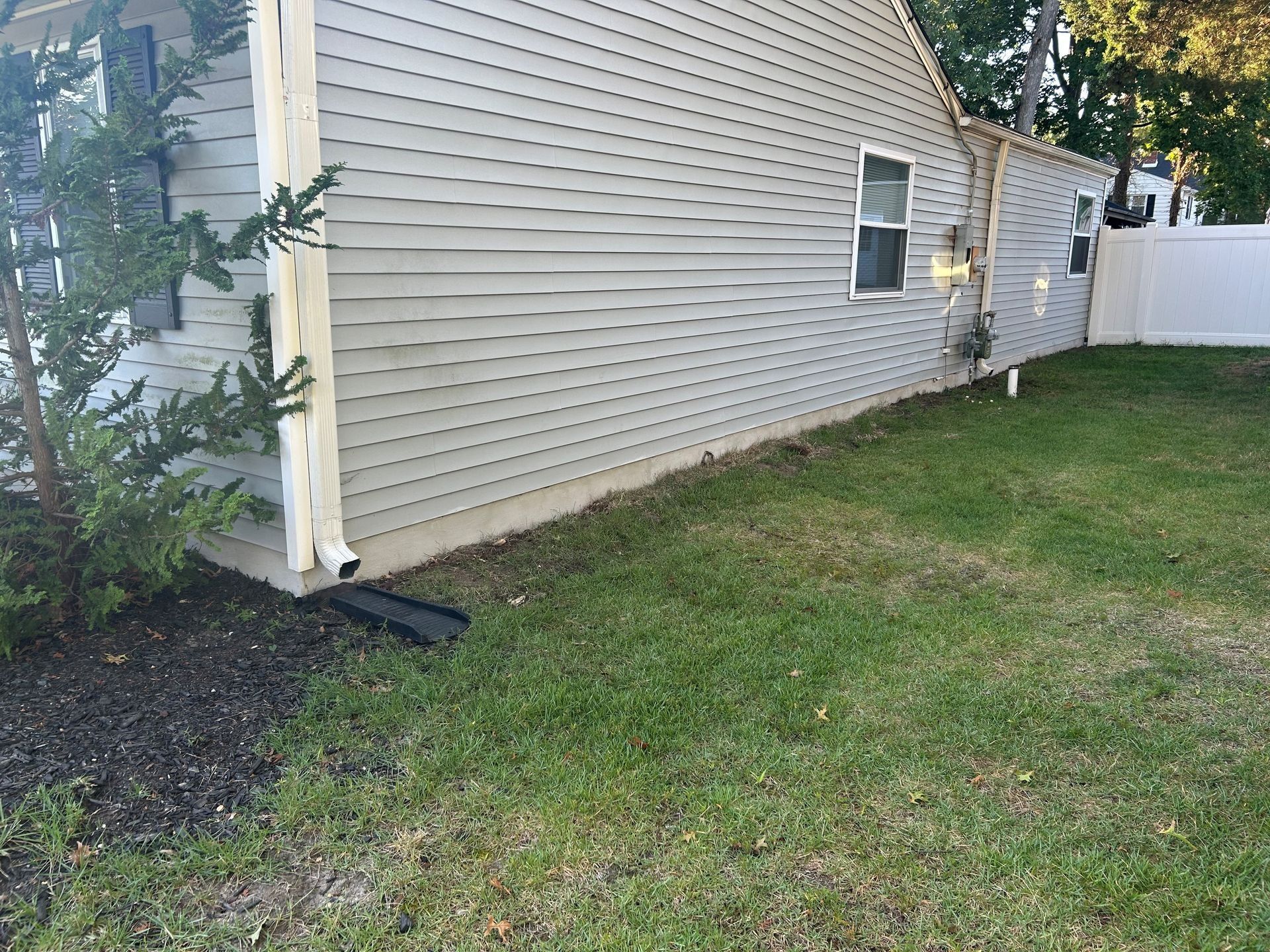 Gray house with white trim, green grass, and a downspout directing water.