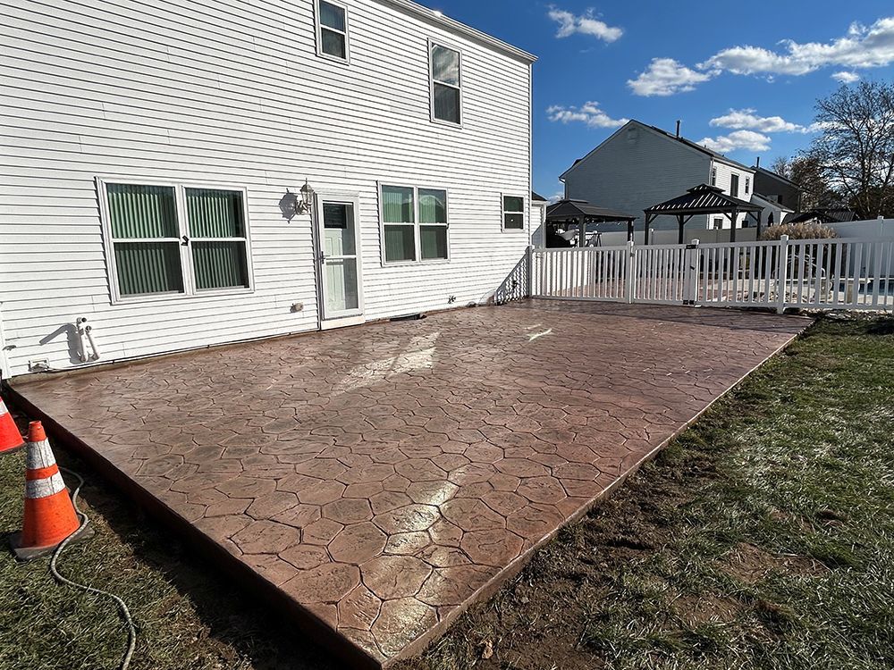 Brown stamped concrete patio next to a white house and fenced backyard.