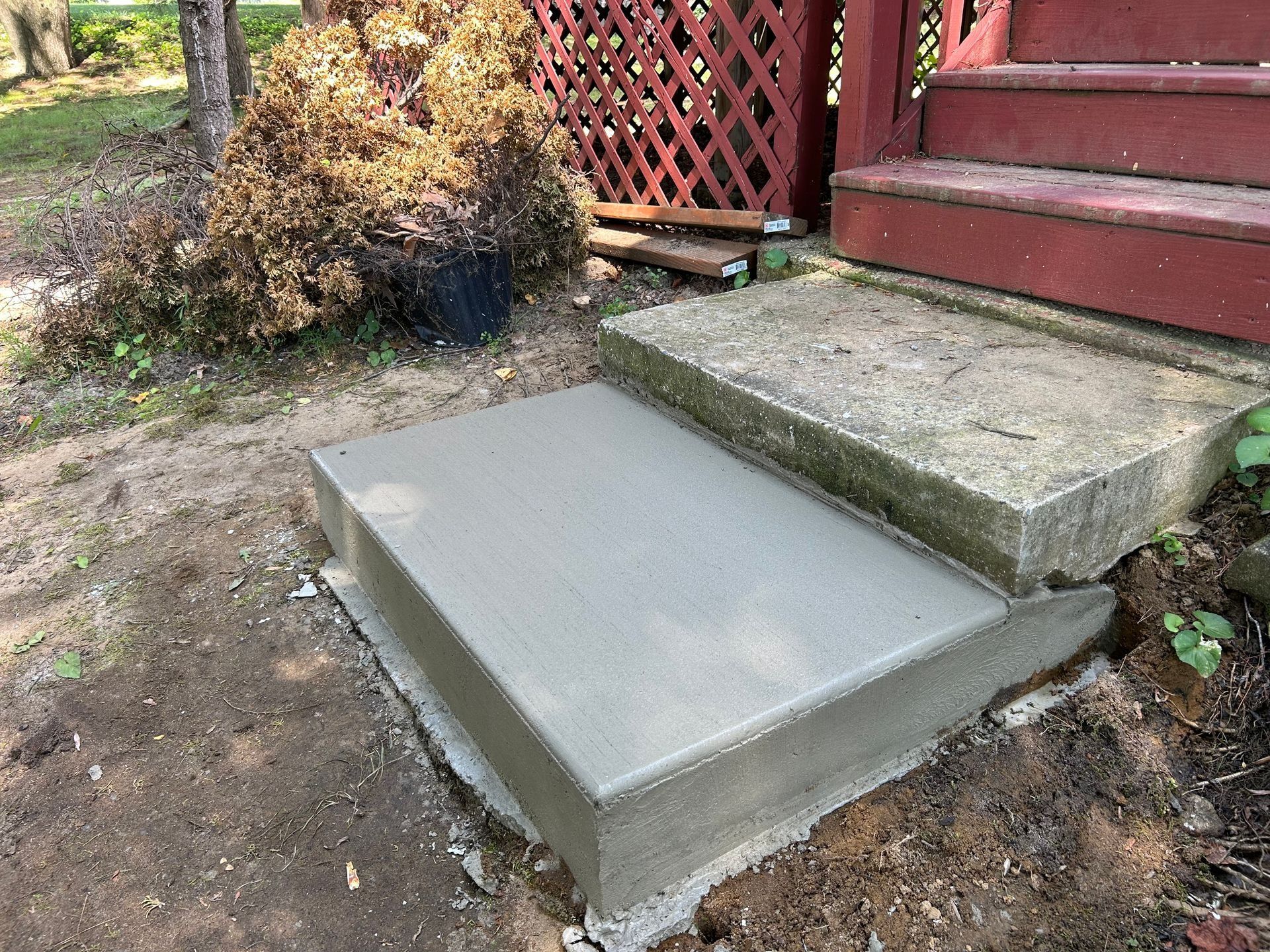 Newly poured concrete step next to an older concrete step, leading to a red porch.