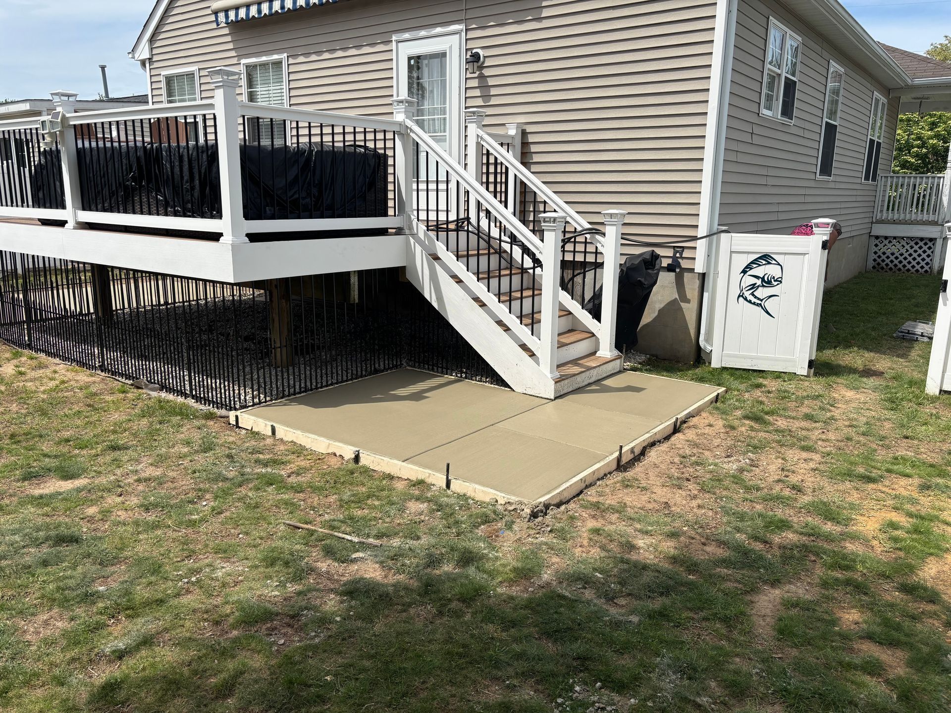 Backyard view of a house with a deck, stairs, and a small concrete patio.