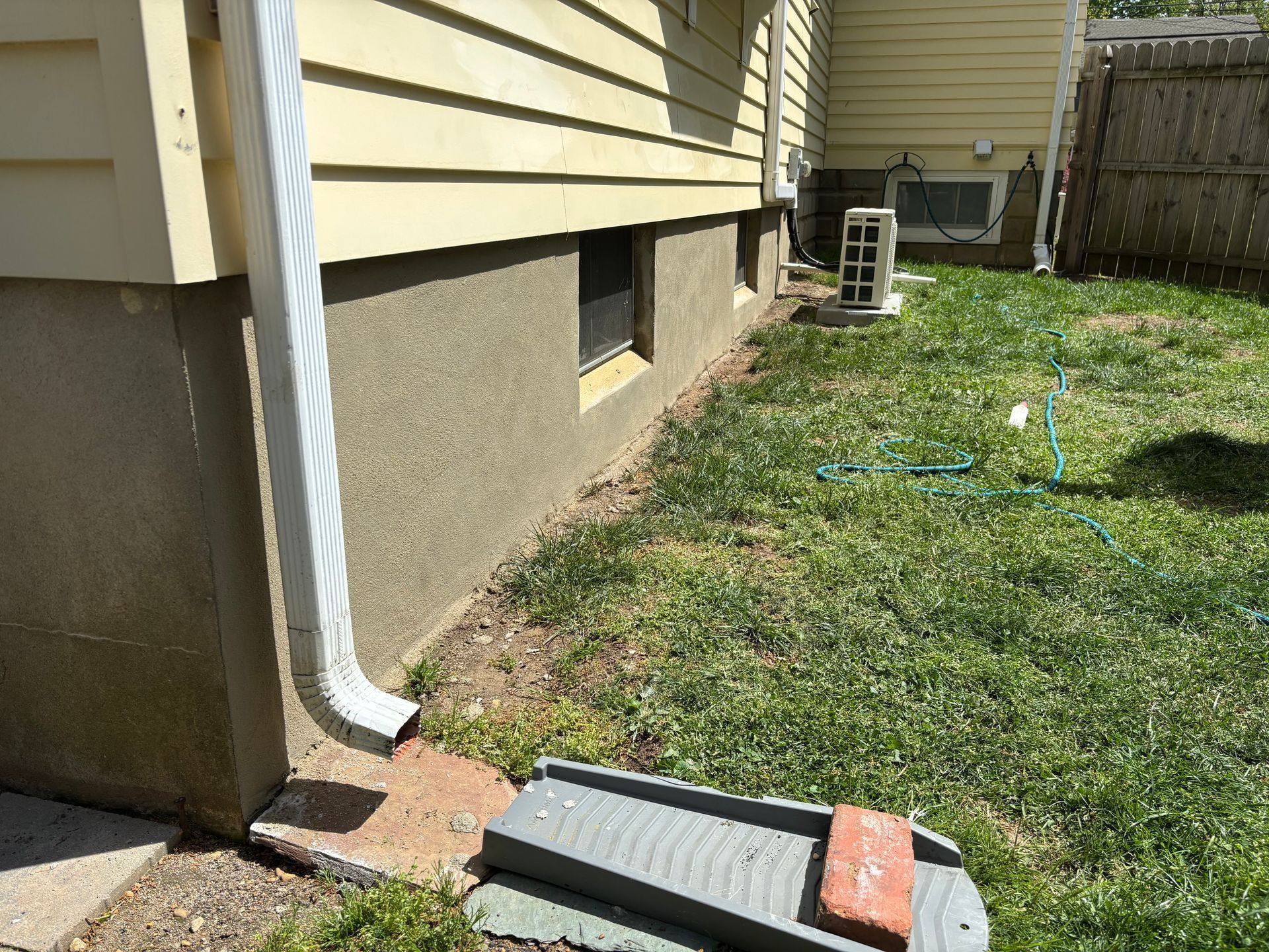 Yellow house with tan stucco foundation, white gutter, small window, and green lawn.