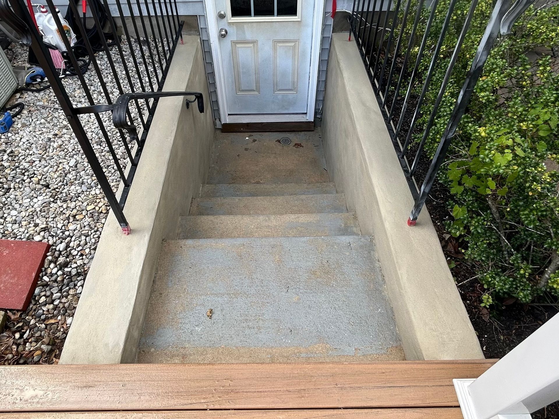 Concrete steps leading down to a doorway, flanked by railings, with a wooden deck in the foreground.