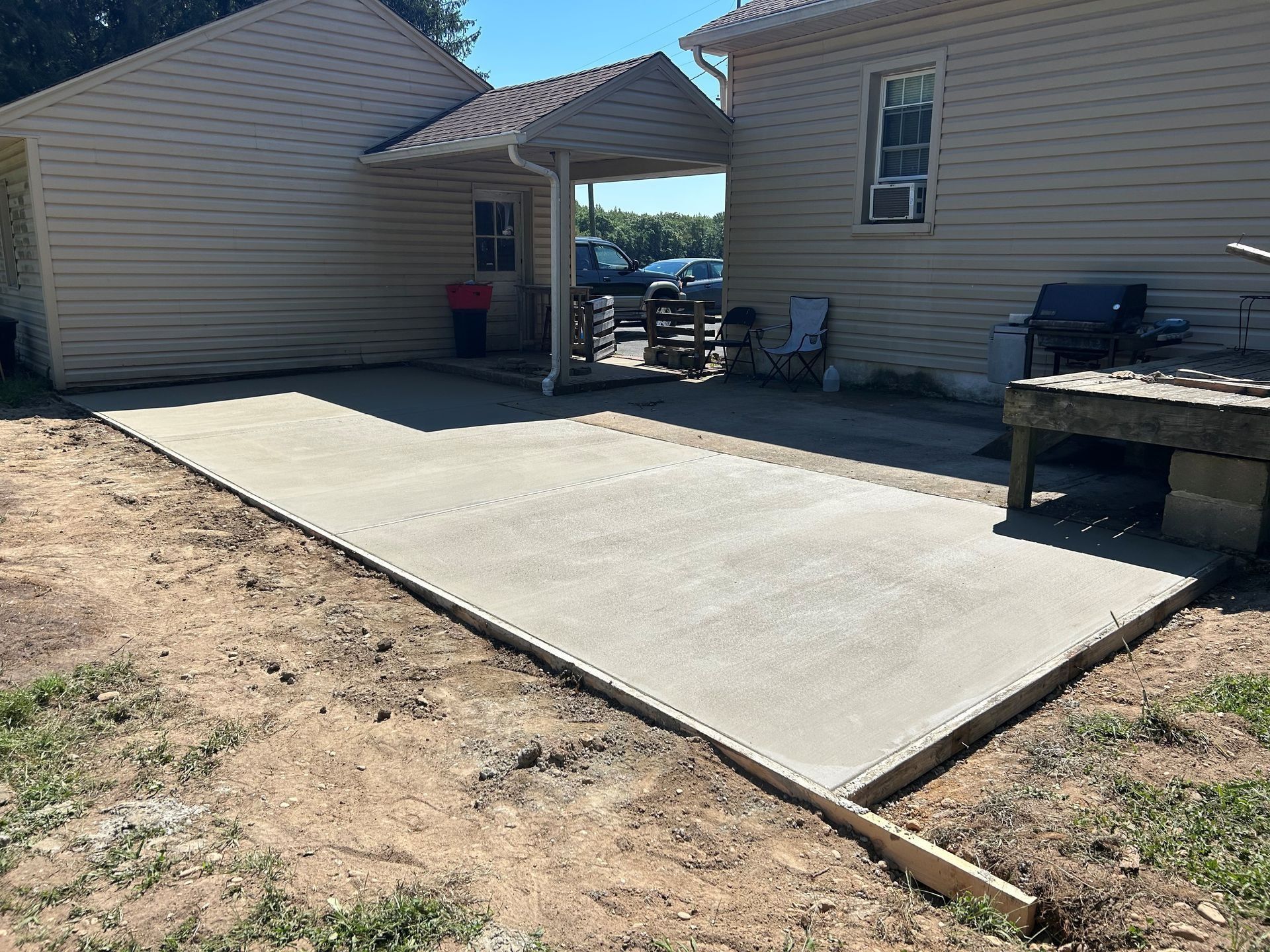 Newly poured concrete patio next to two beige houses, set in a yard.