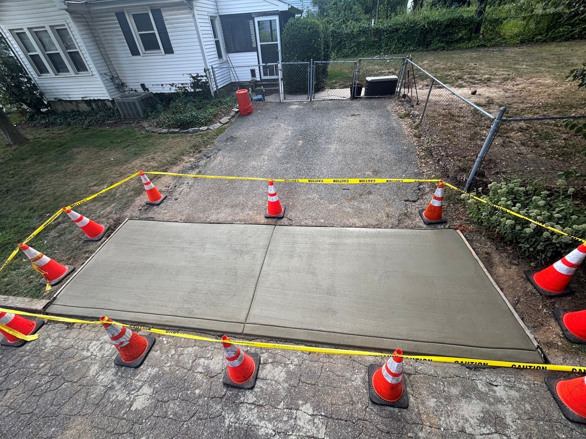 New concrete sidewalk section in a driveway, cones and caution tape.