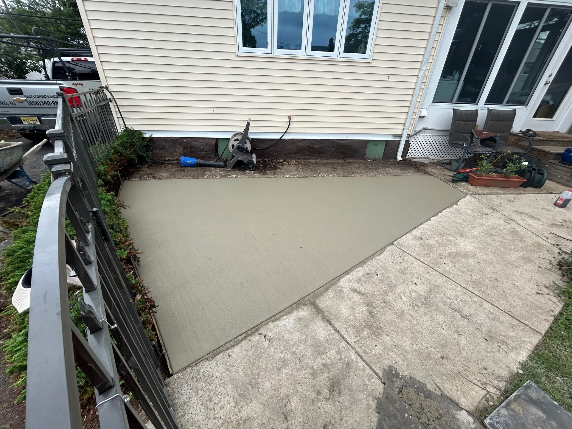 Newly poured concrete patio adjacent to a house and existing walkway.