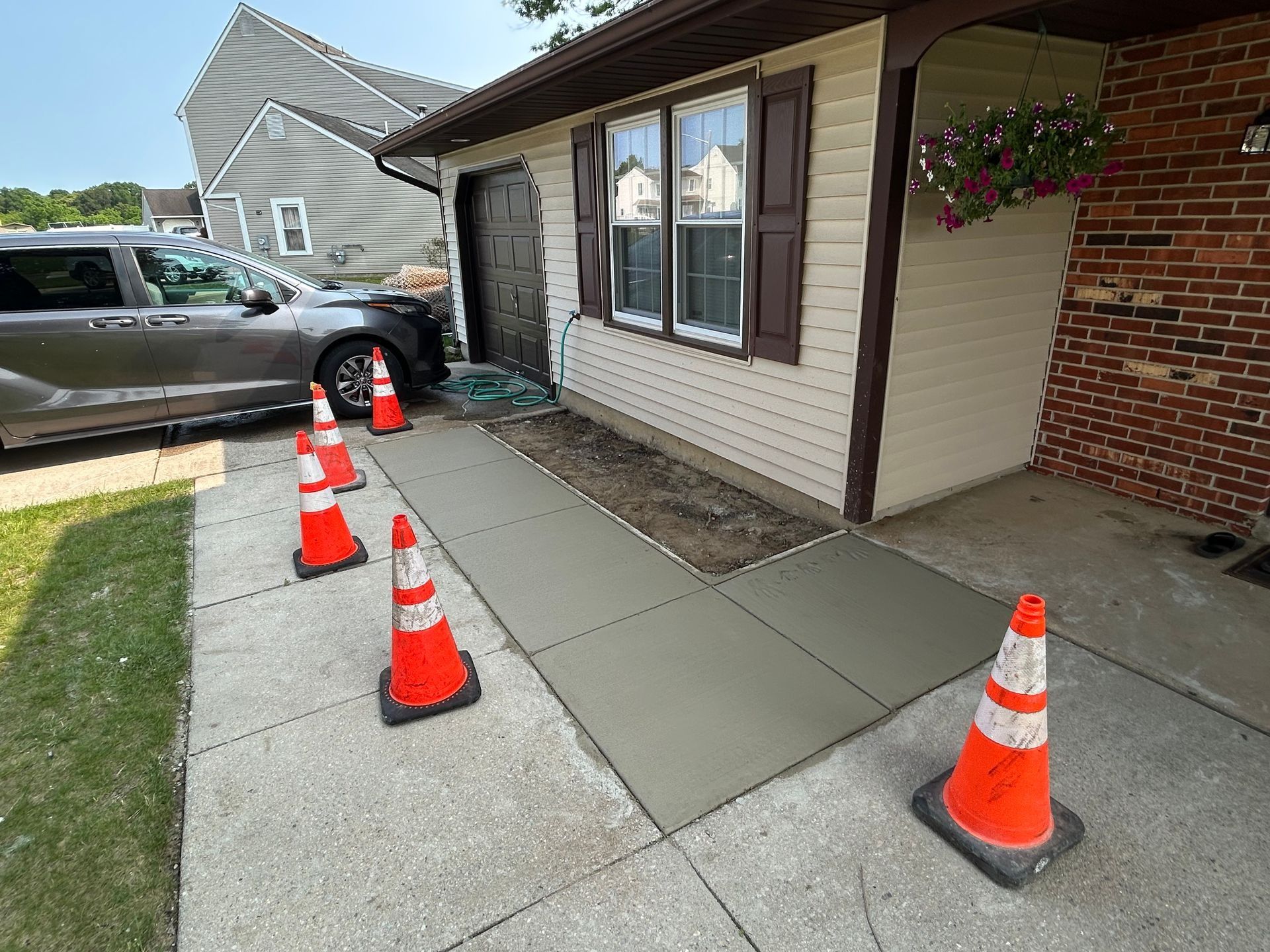 Newly poured concrete ramp with orange cones, next to a house with a garage.