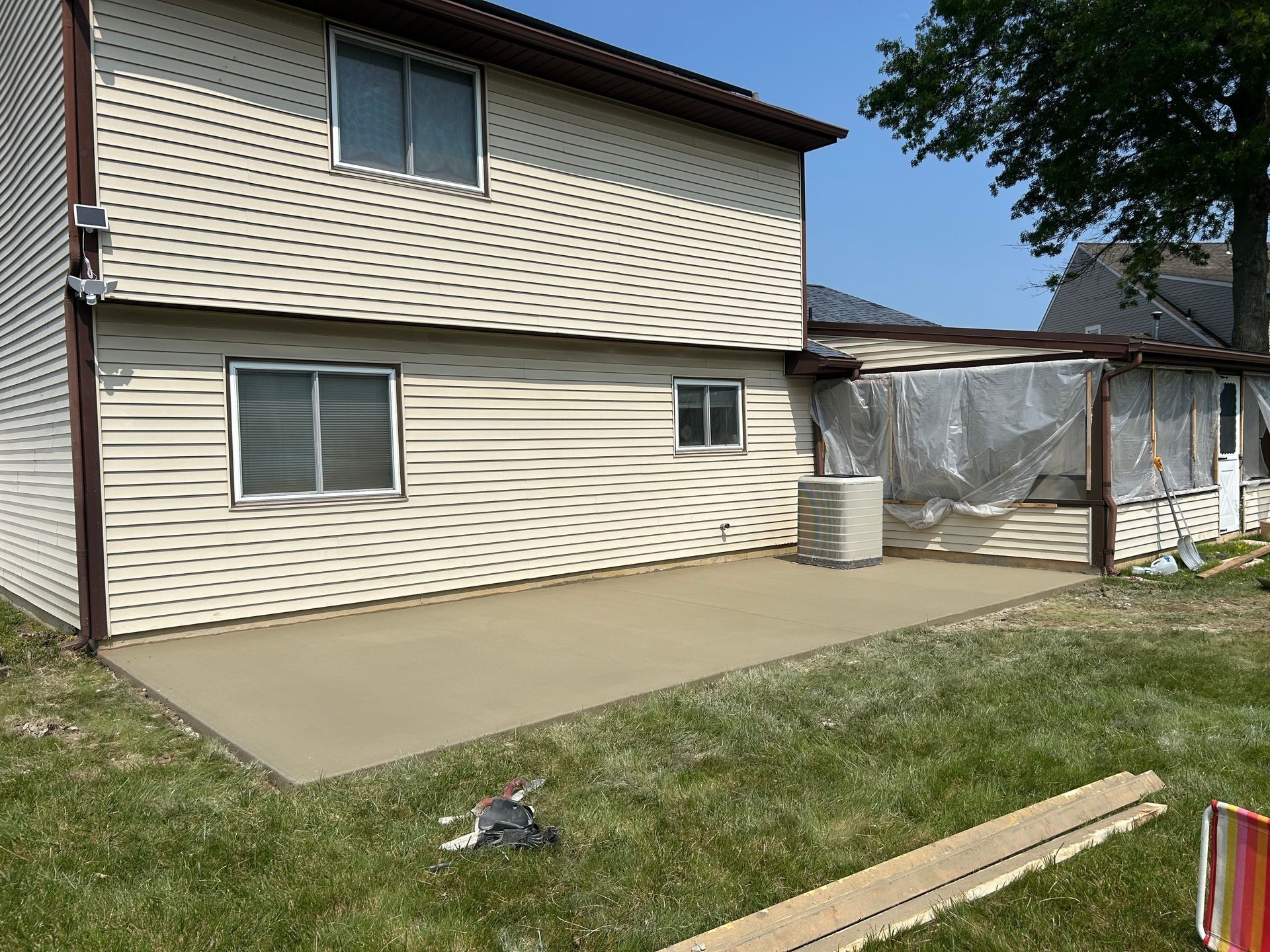 A freshly poured concrete patio extends from a beige house with a partially covered outdoor area.