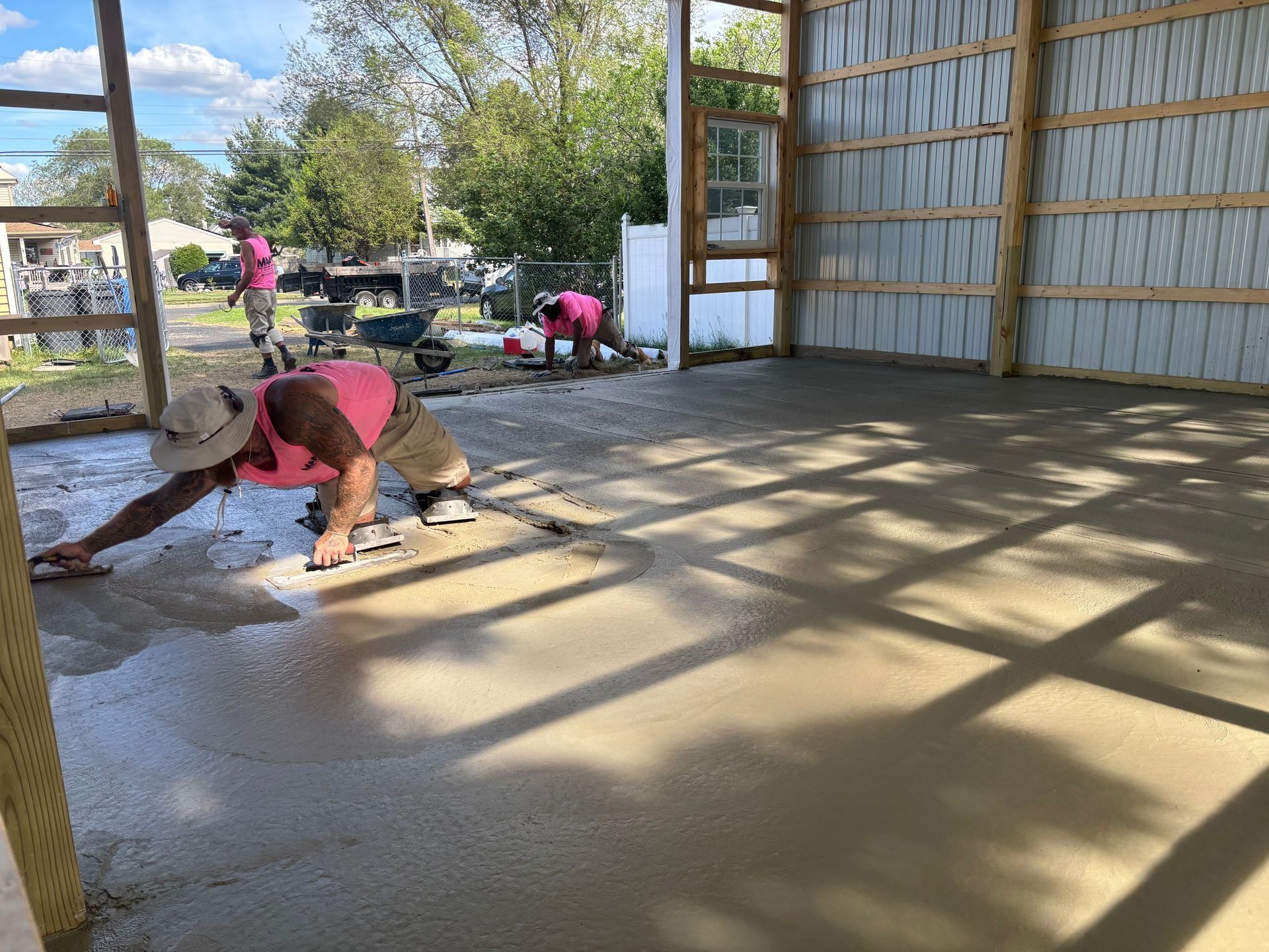 Workers in pink shirts smoothing wet concrete floor inside a barn.
