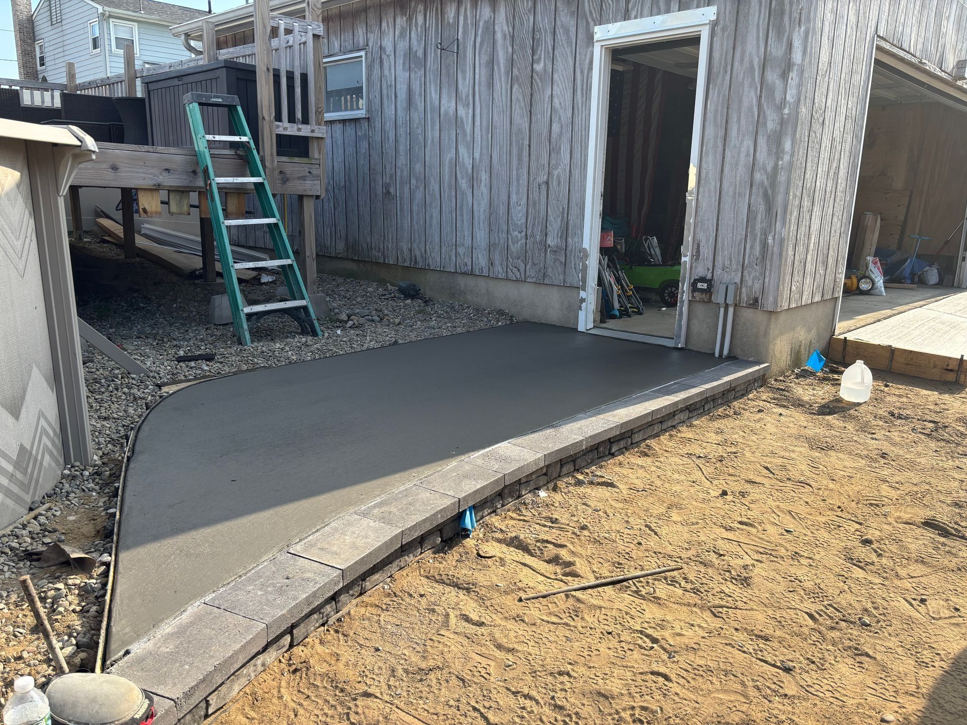 Newly poured concrete patio with a brick border next to a weathered wooden garage.