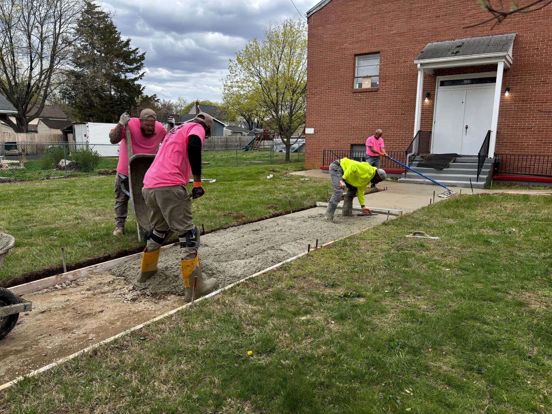 Construction workers pouring concrete for a sidewalk in front of a brick building.