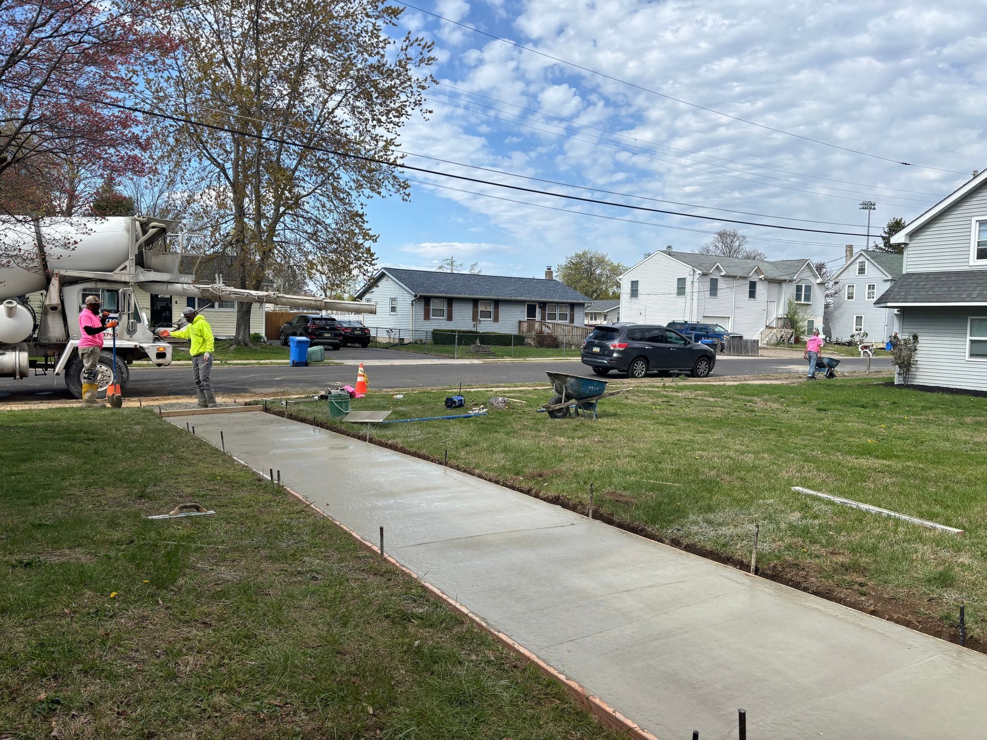 Concrete sidewalk being poured on a residential street. Workers and cement truck are present.