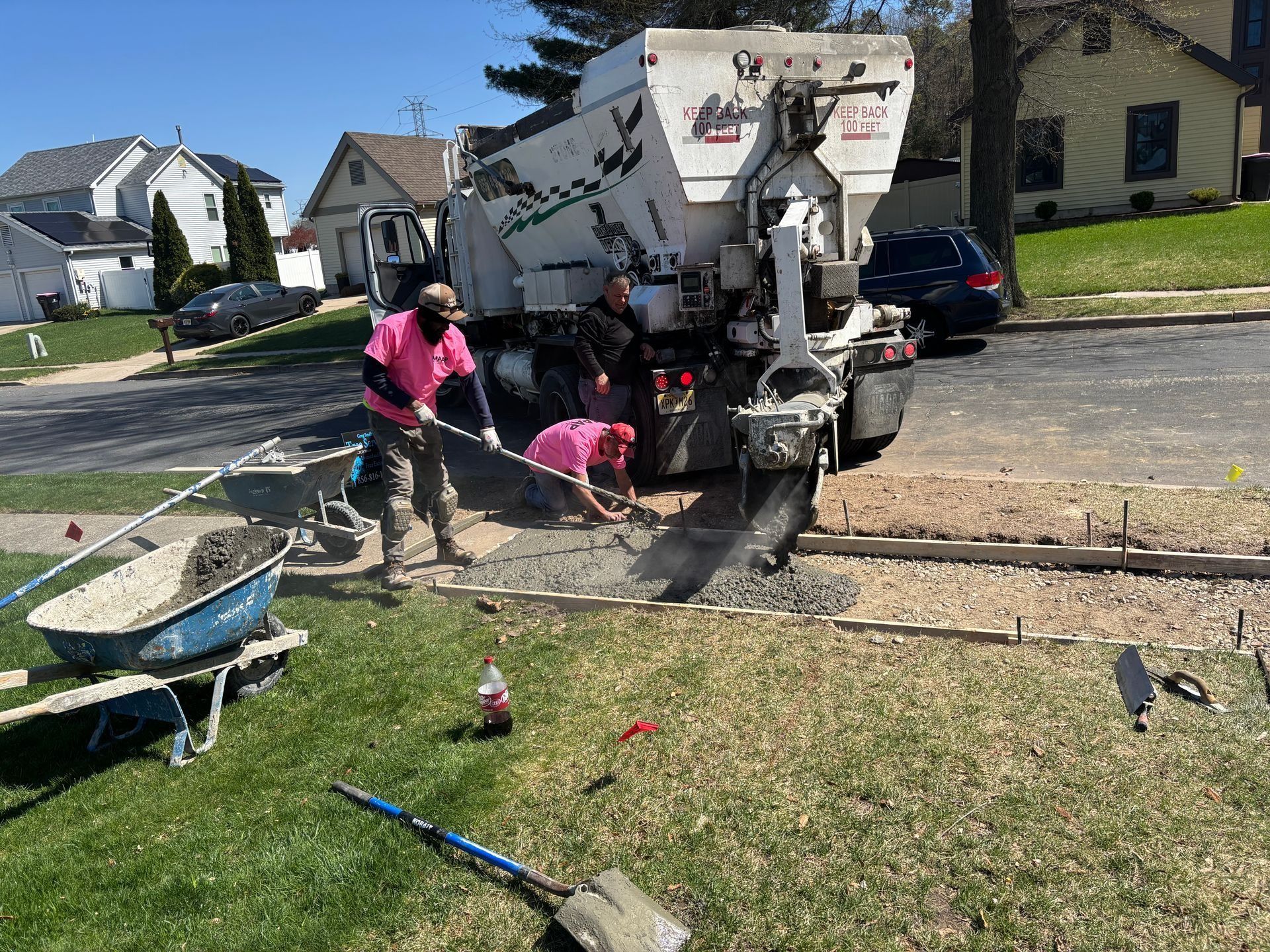 Workers pouring concrete from a cement truck for a sidewalk in a residential area.