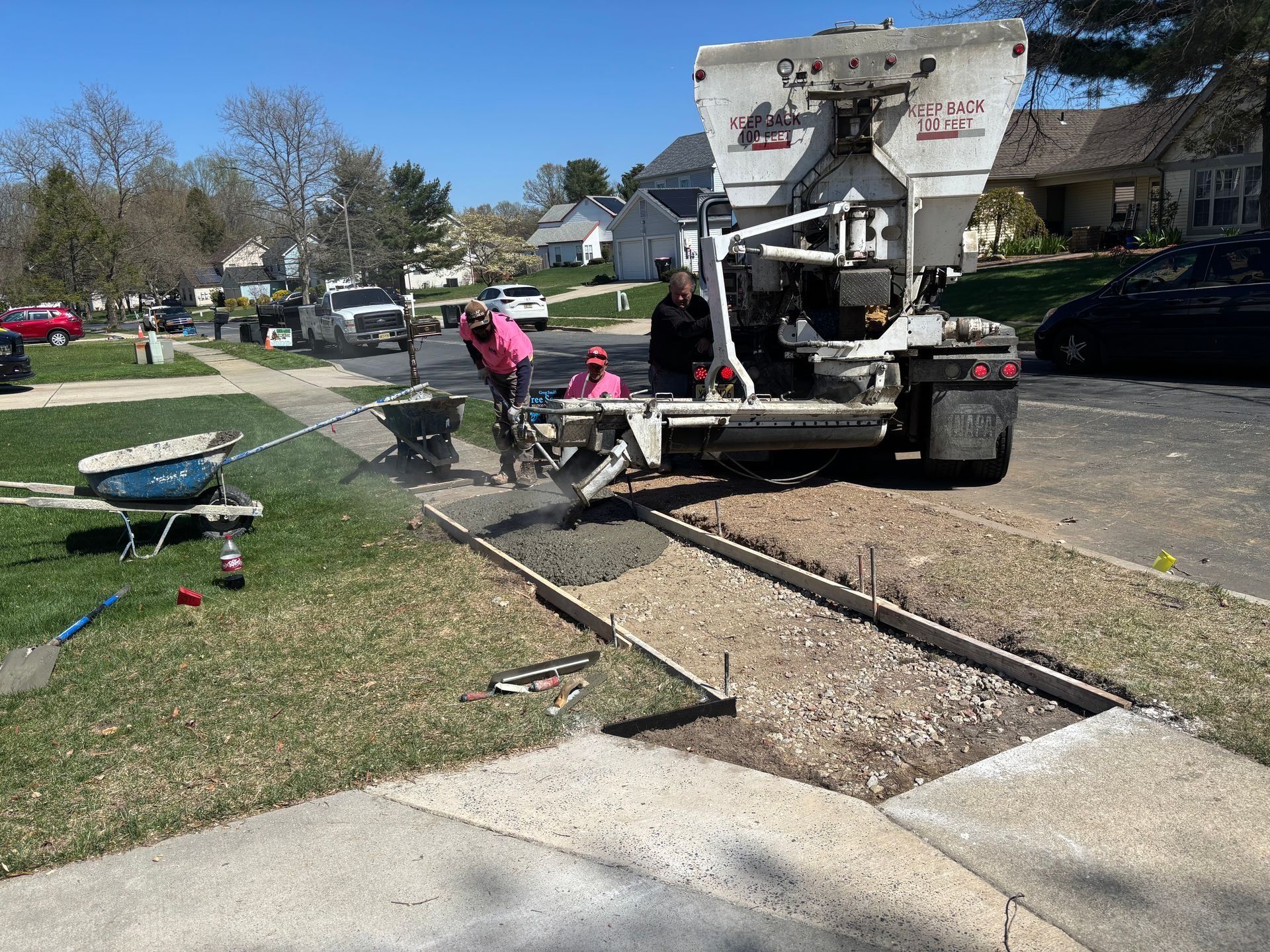 Concrete truck pouring concrete into a sidewalk form with workers; residential street.