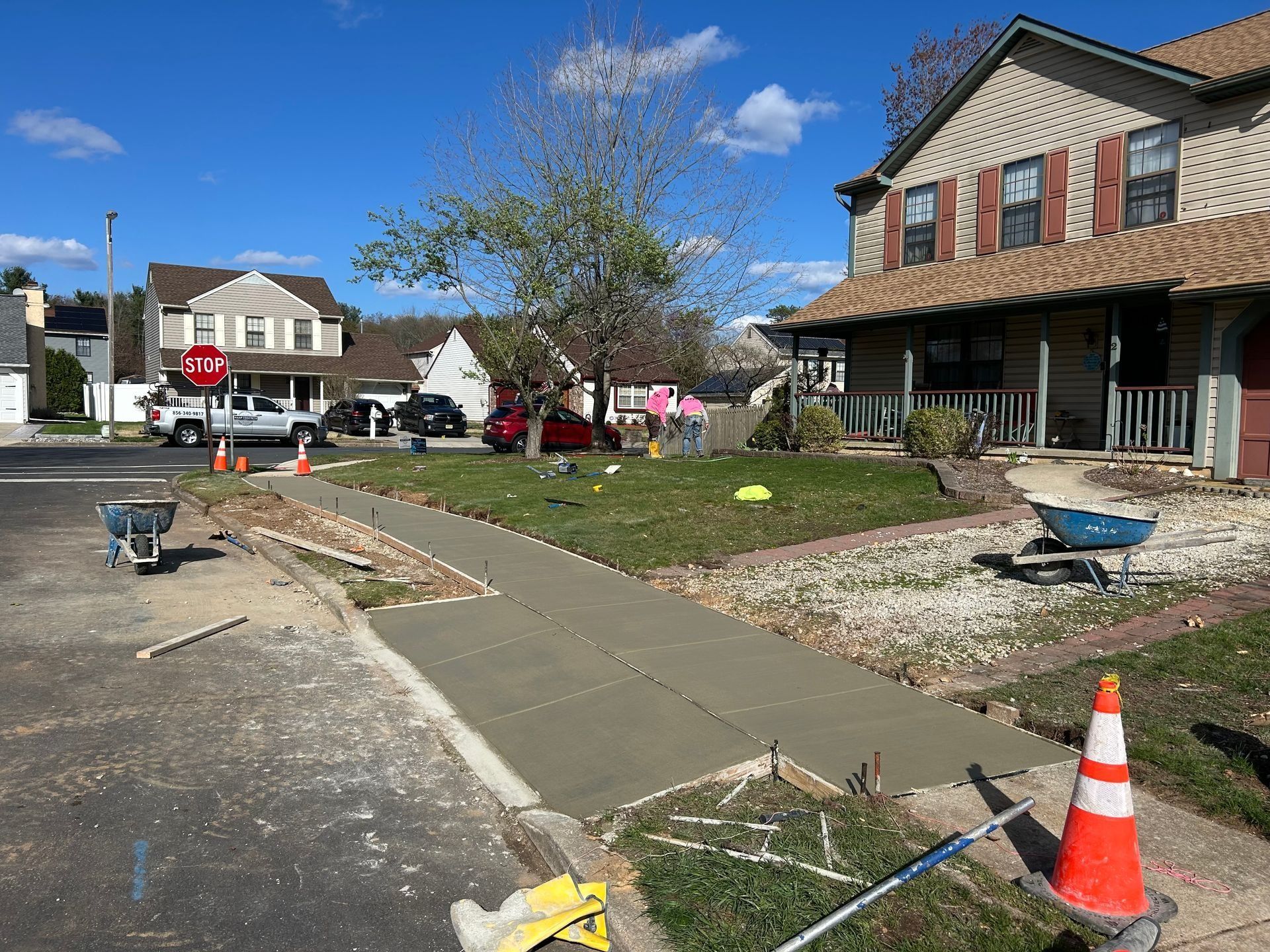 Newly poured concrete sidewalk in front of a house; construction cones and equipment are visible.
