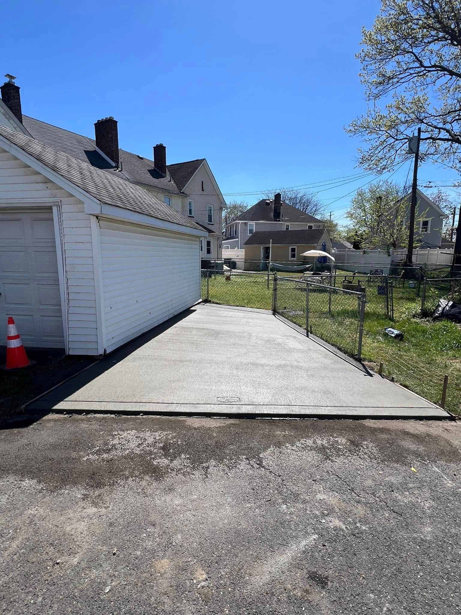 Newly poured concrete pad next to a white garage under a bright blue sky.