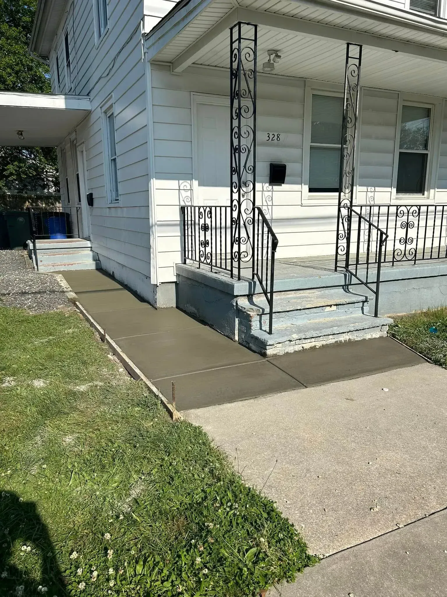 Exterior of a white house with a new concrete ramp leading to the porch. Green grass surrounds.