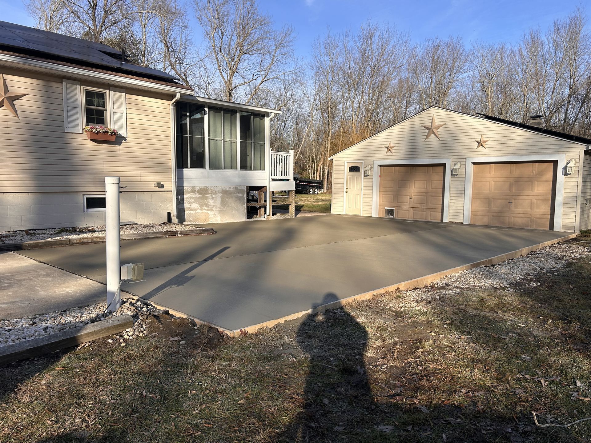 Newly poured concrete driveway between a house and detached garage on a sunny day.