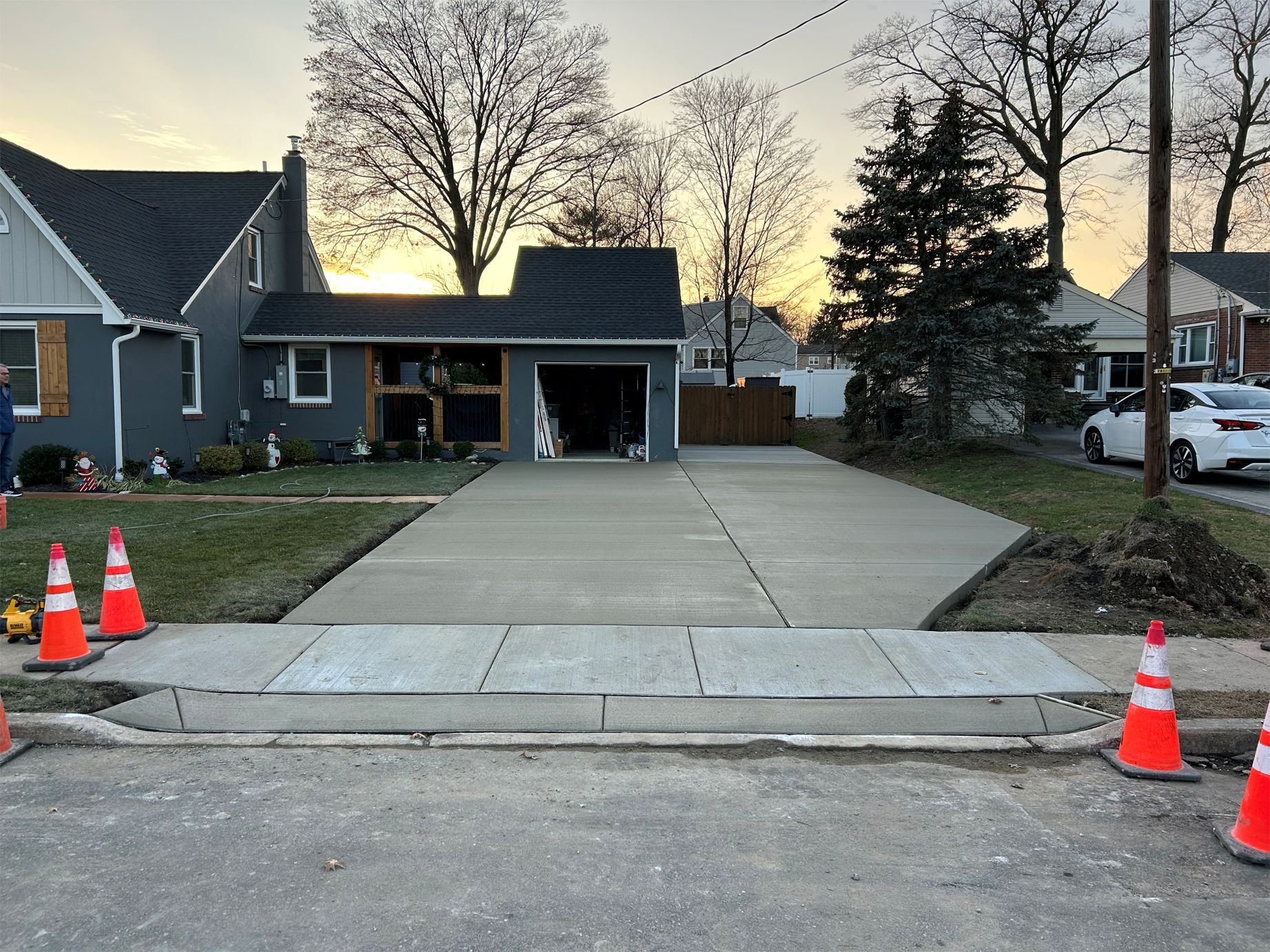 Concrete driveway with orange cones and house with garage in background. Evening setting.