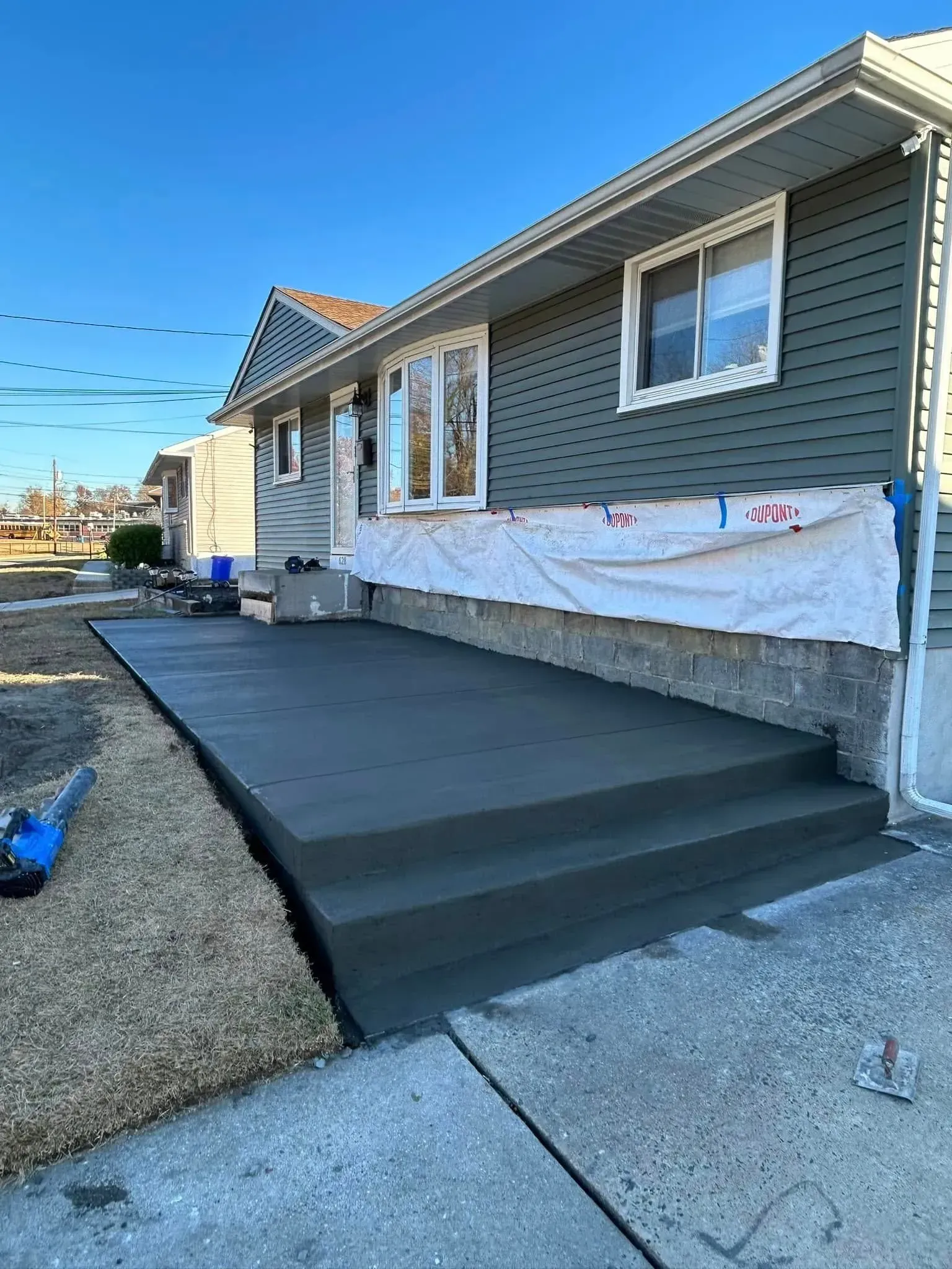 Newly poured concrete porch and steps in front of a house with green siding, under construction.