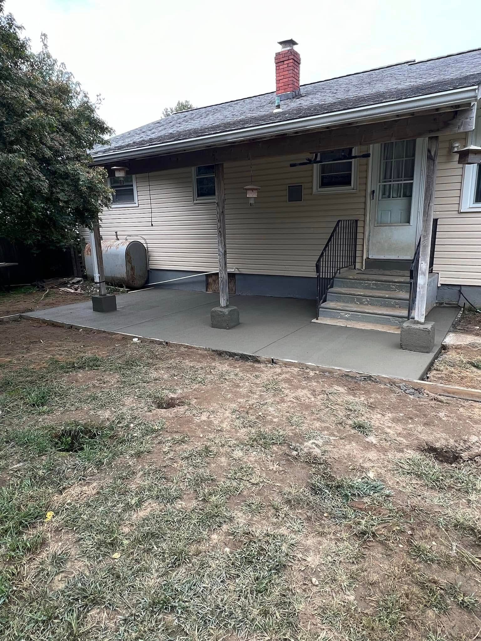 Newly poured concrete patio under a house with steps, supported by wooden posts.