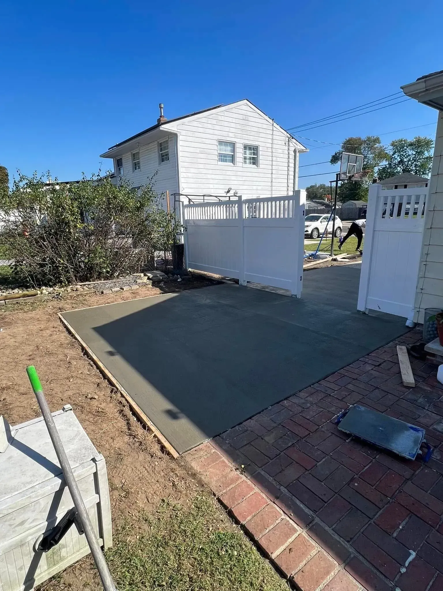 Fresh concrete patio being poured in a backyard. A white fence and house are in the background.